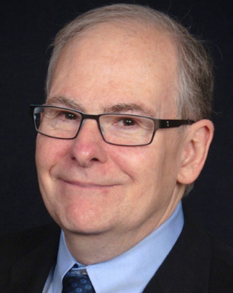 A man in glasses, a dark suit jacket and a light blue dress shirt