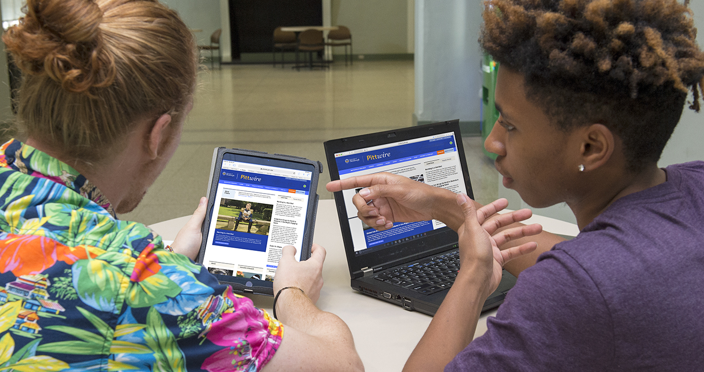 Two male students reading PIttwire online, one on a tablet and the other on a laptop computer.