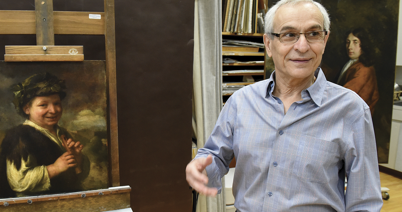 Costas Karakatsanis, wearing blue button down shirt with books/manuscripts and paintings in the background