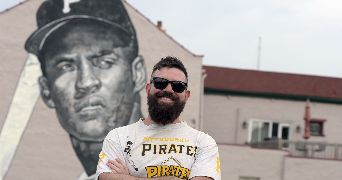 Pitt alumnus Jeremy M. Raymer in a PIttsburgh Pirates shirt standing in front of a mural he painted of Pirates baseball player Roberto Clemente