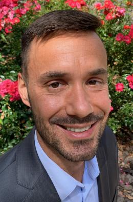 Rogers in a suit and tie in front of a flowering bush