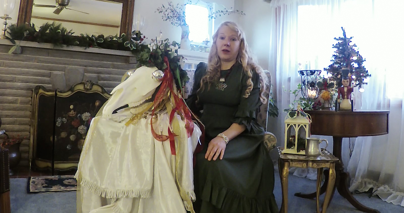 A woman in a green dress sitting in a chair next to a white skull with decorations on it, on a table