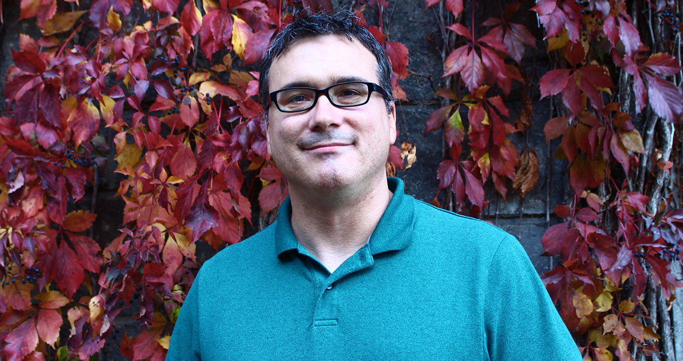 Shawn Brown in a teal collared shirt against a dark red floral background