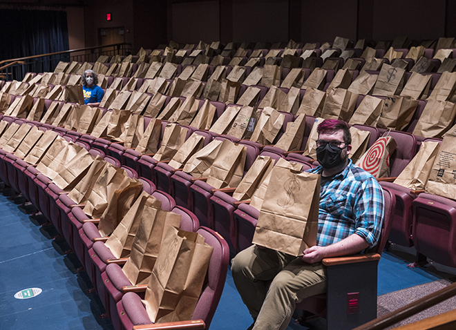 two people sitting a row and a dozen seats apart in theater seats