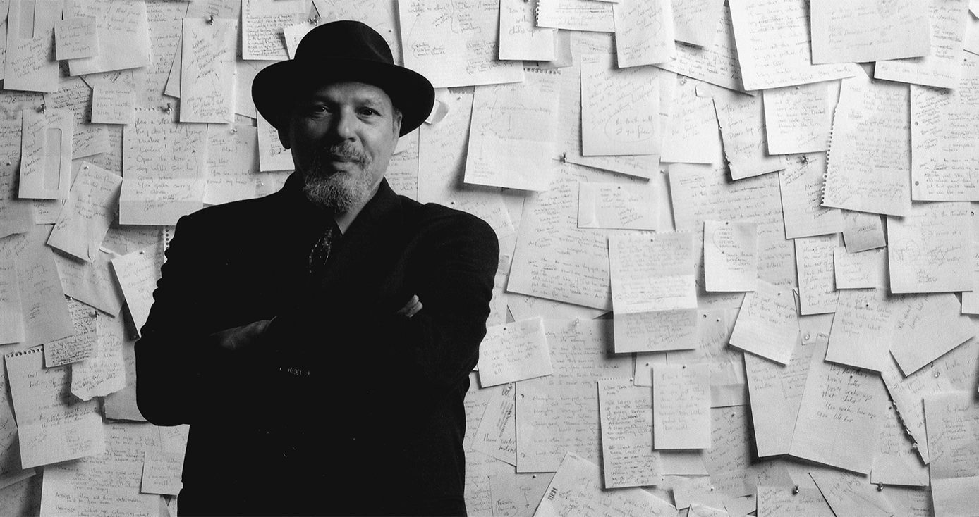 a black and white photo of Wilson standing in front of a wall covered in handwritten pages