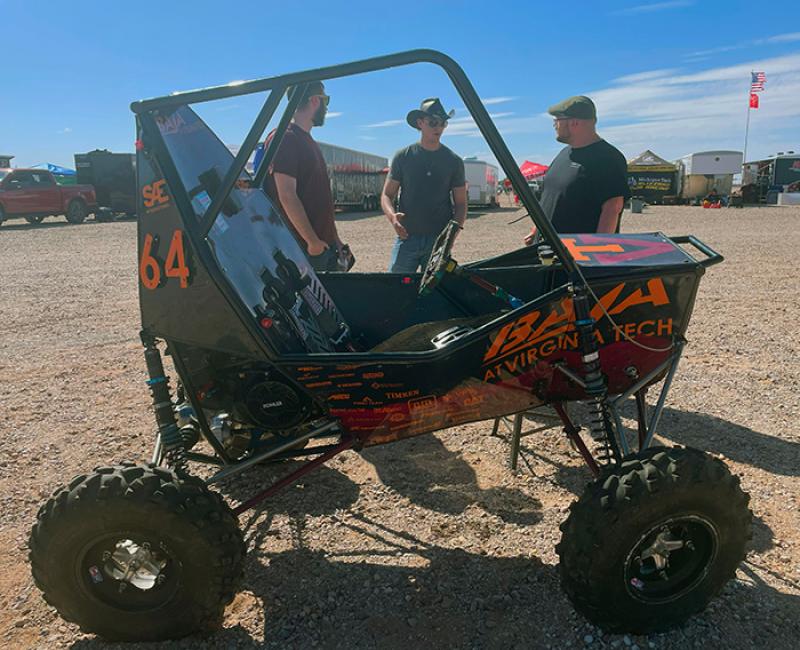 Students stand by a buggy-like car in the desert.