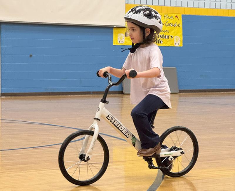 A kindergartener in a helmet rides on a bike in a gym court