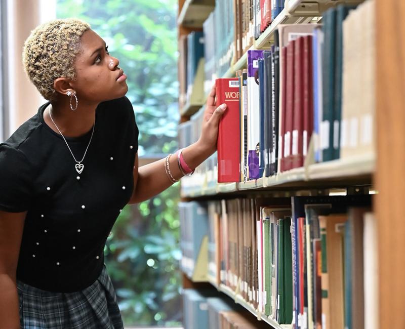 A student pulls a book from a library shelf.