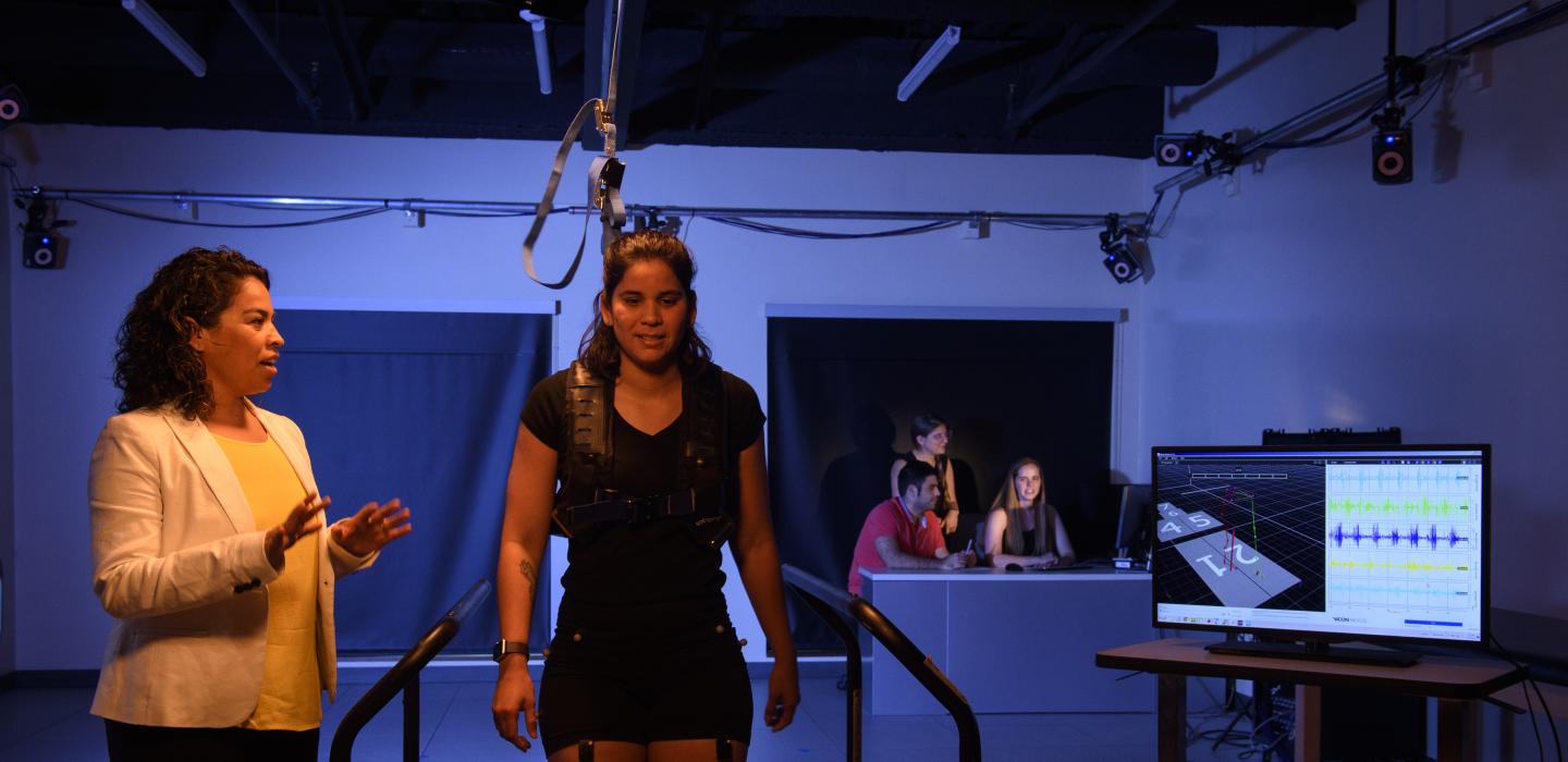 a person on a treadmill attached to ropes above with a person standing next to her