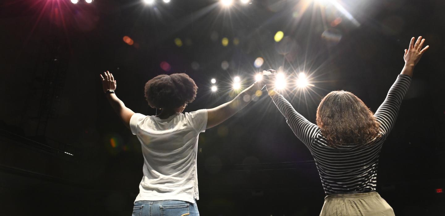 Two women holding hands in a spotlight