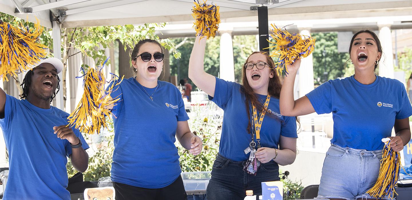Four Pitt students wearing matching blue Pitt shirts cheering