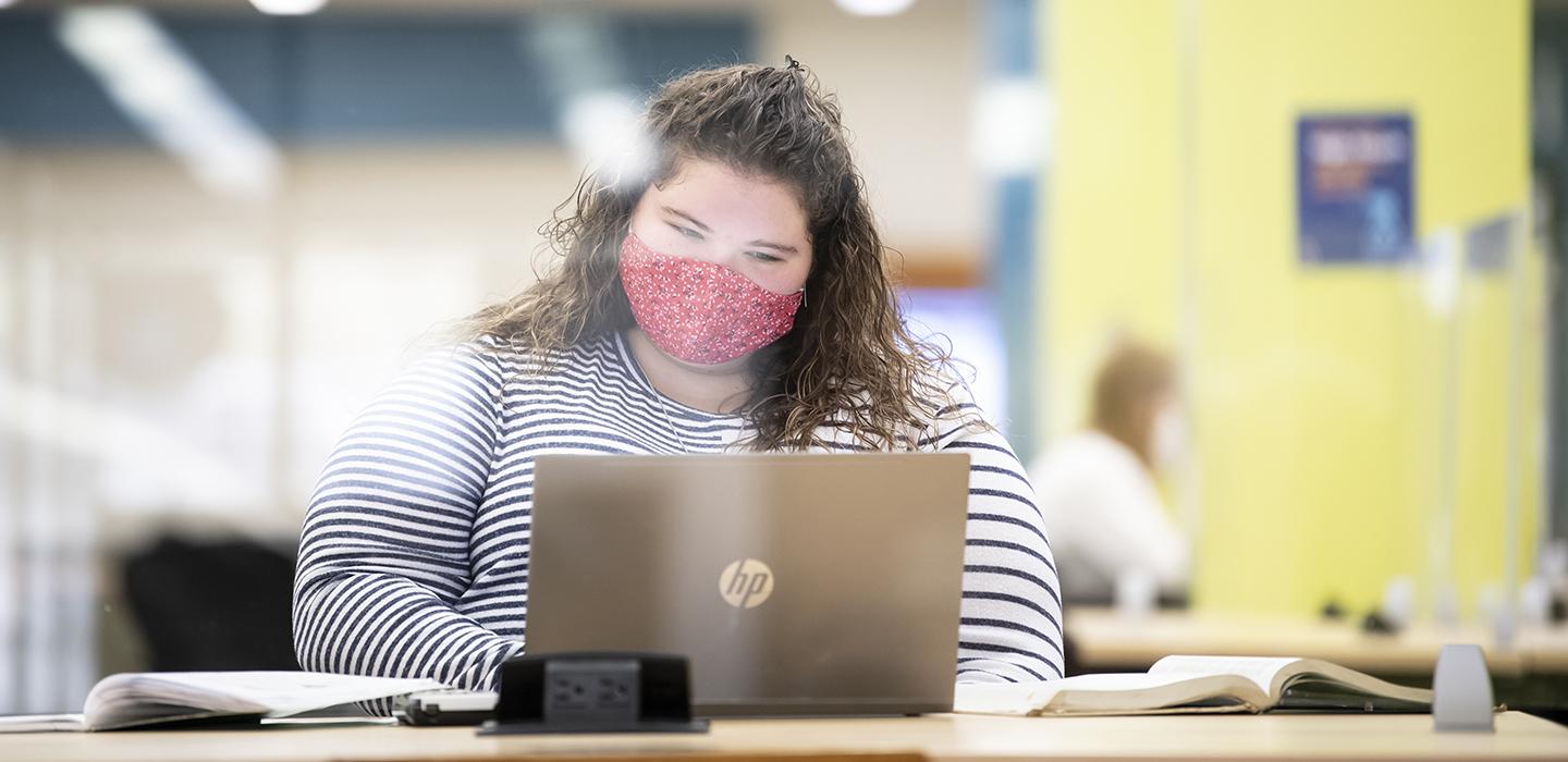 Student with red mask working on laptop 