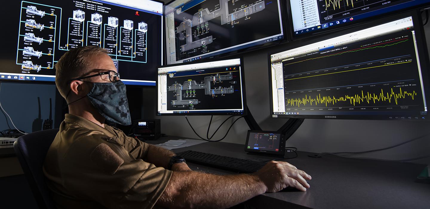 Man with mask using computer with five monitors