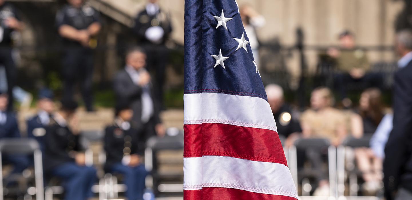 an American flag in the foreground with people gathered in the background