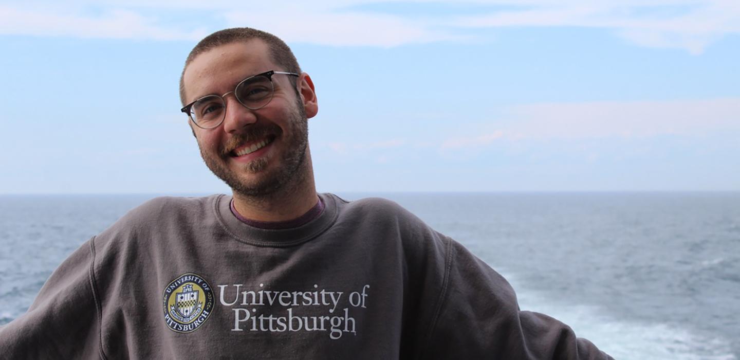Brett Bankson smiling with grey Pitt sweater, ocean in the background