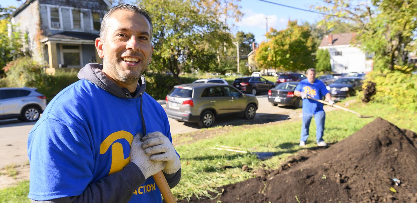 Two men with blue Pitt shirts digging dirt from ground.