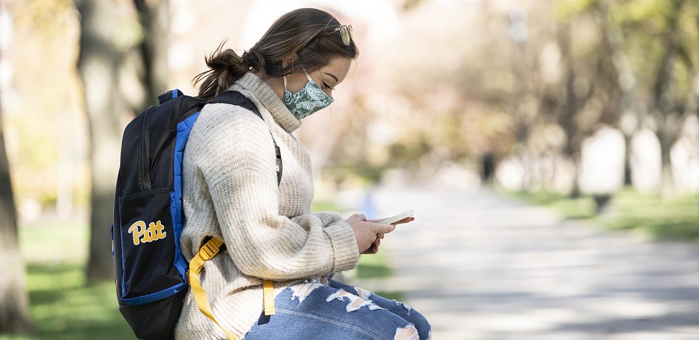 Student sitting outside on a bench using cell phone