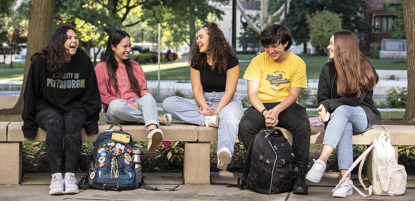 Latinx students sitting together outside with bookbags