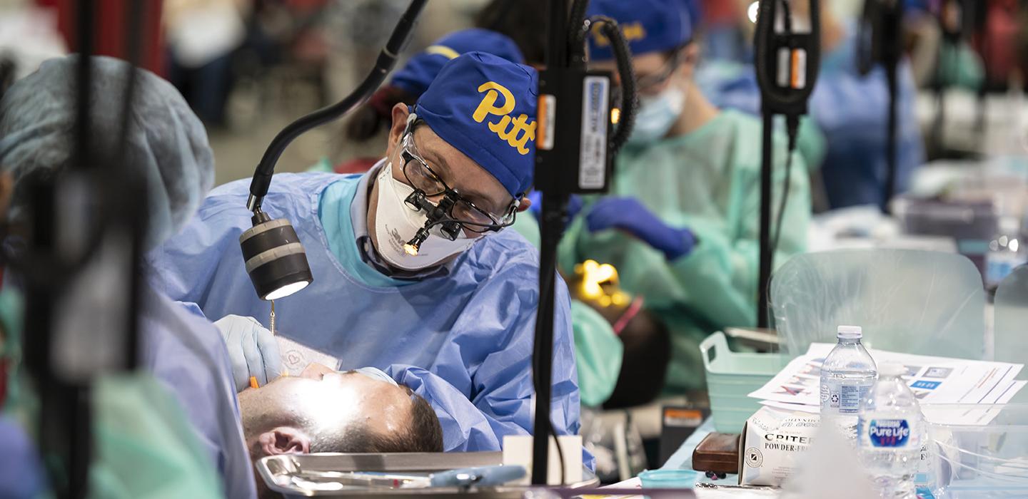 Pitt dentist wearing blue and gold Pitt cap working on patient
