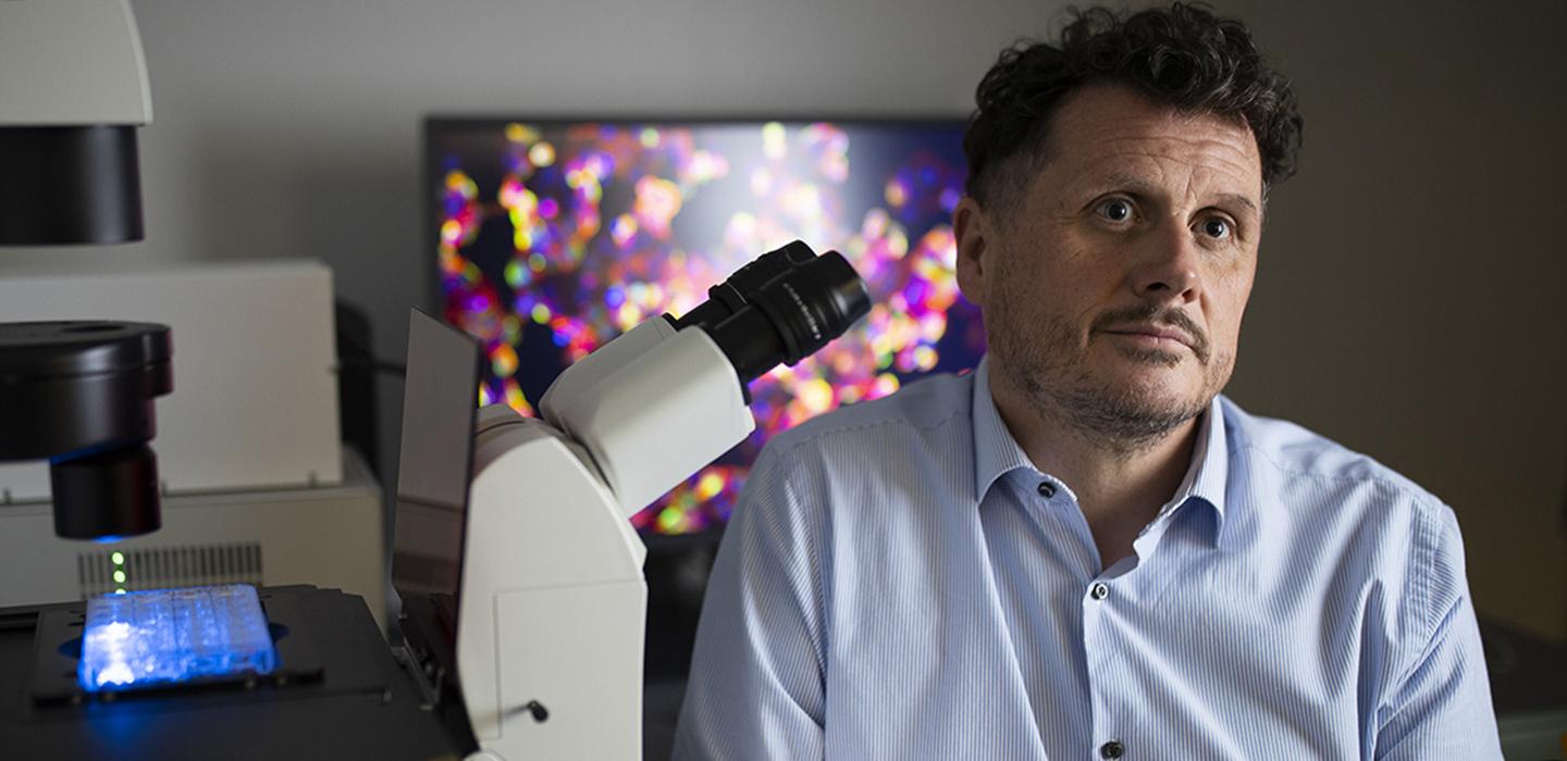 Paul Duprex sitting next to microscope 