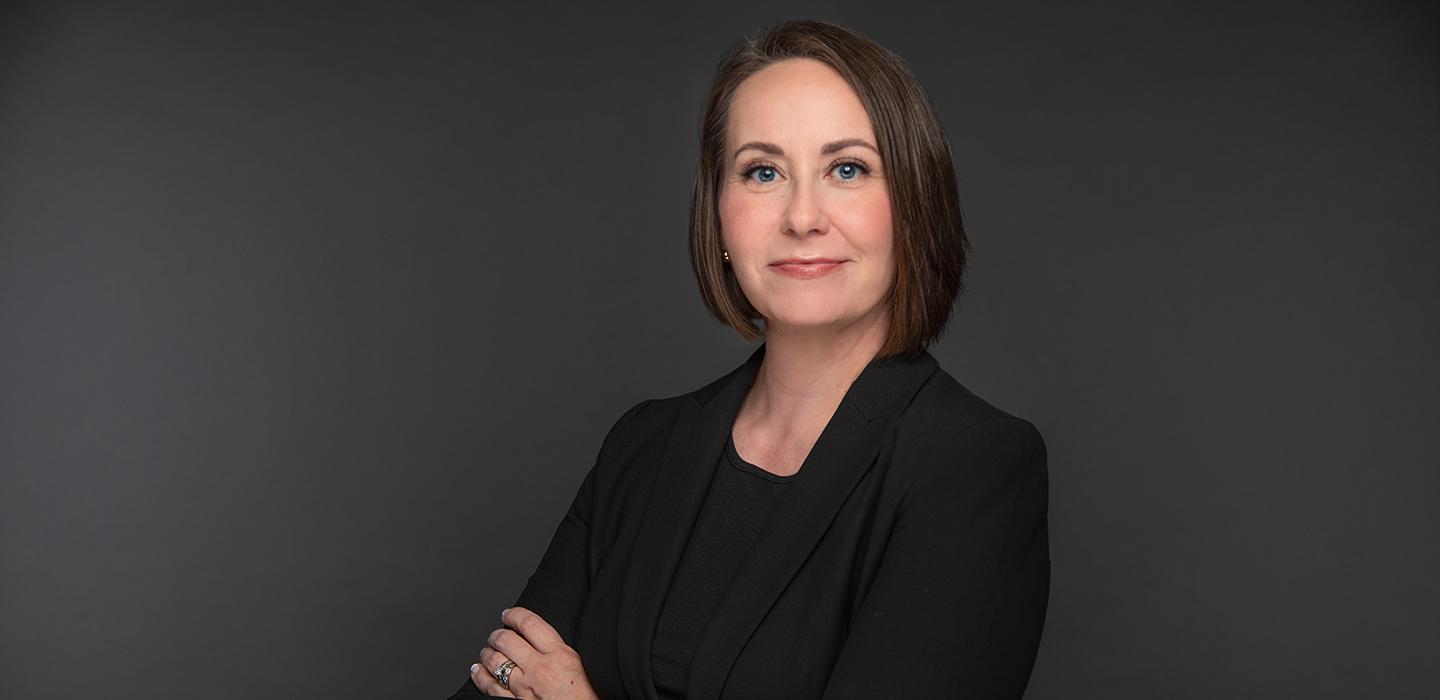 Lina Dostilio smiling with arms folded in front of grey background