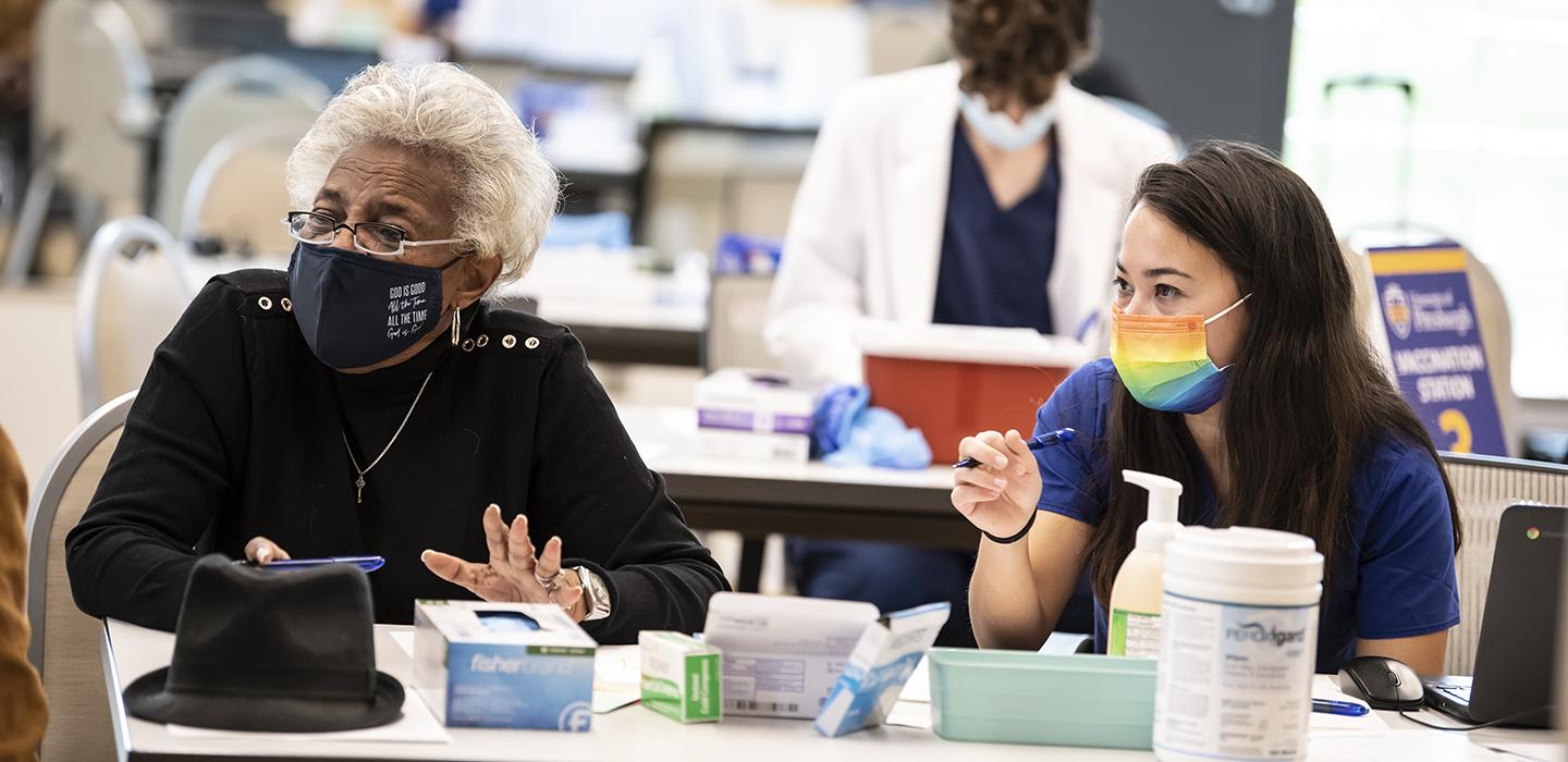 Two women with masks sitting at table at vaccine clinic