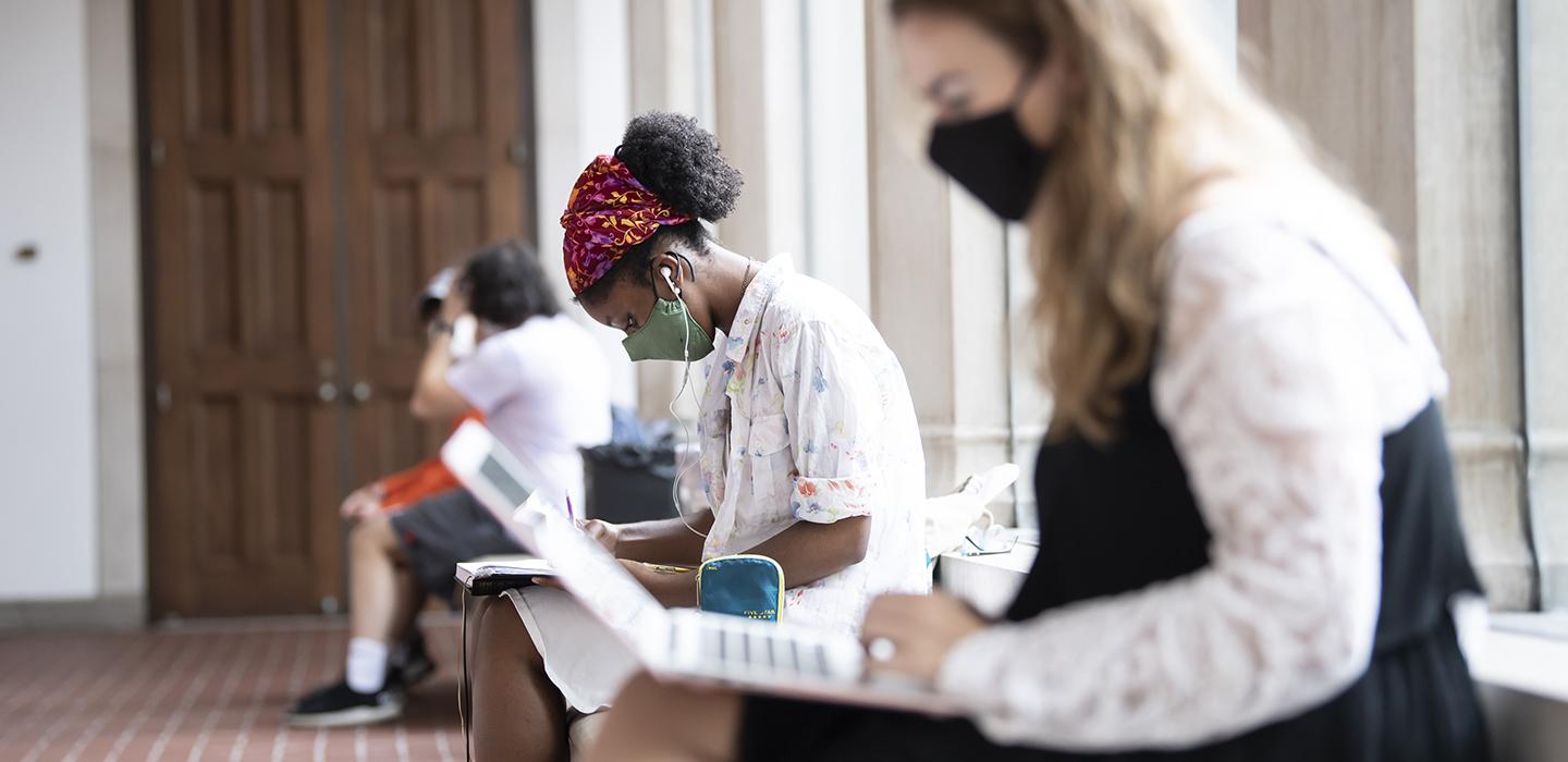 Multiple Pitt students with face masks studying separately on a long bench 
