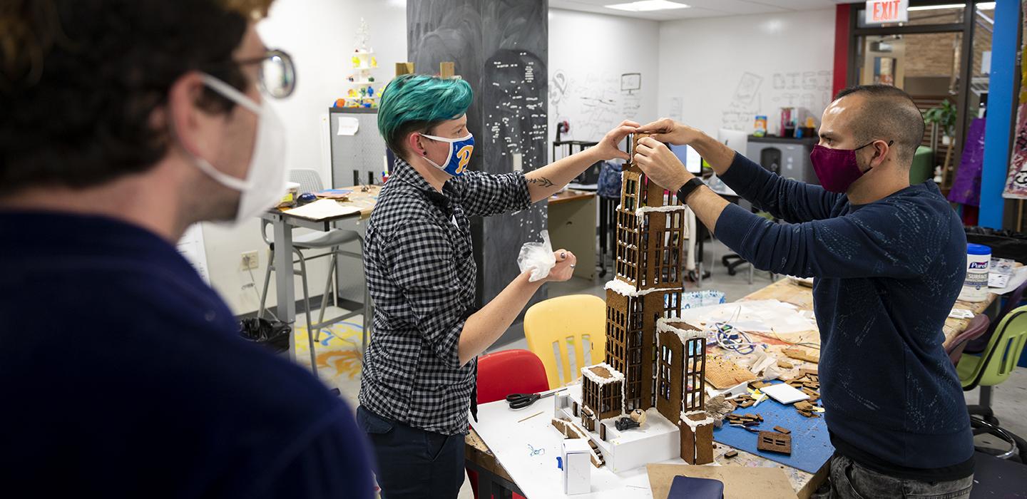 Students with face masks carefully building gingerbread Cathedral of Learning