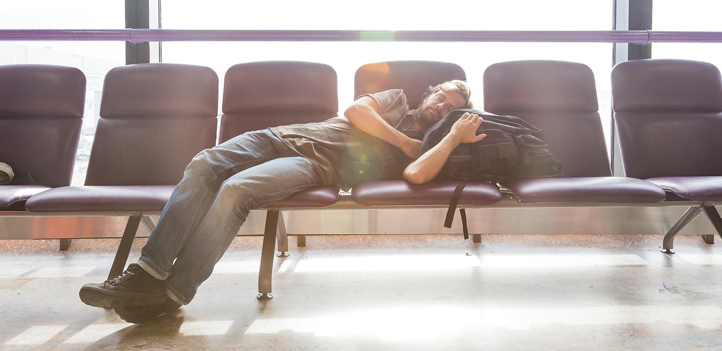 Man sleeping on chairs with head on backpack in airport