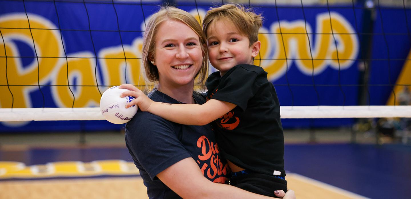 Molly Trott holding Daniel George on Pitt volleyball court