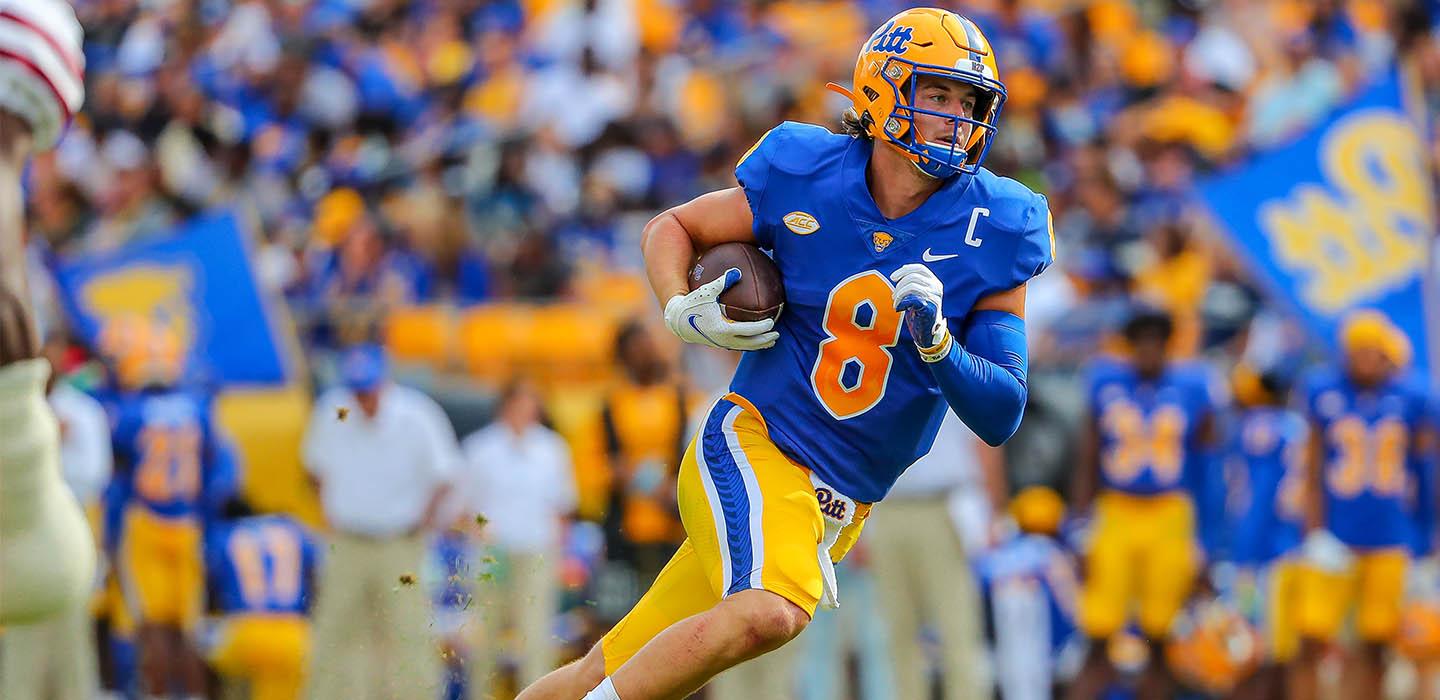a quarterback in blue and gold with the ball tucked under his arm