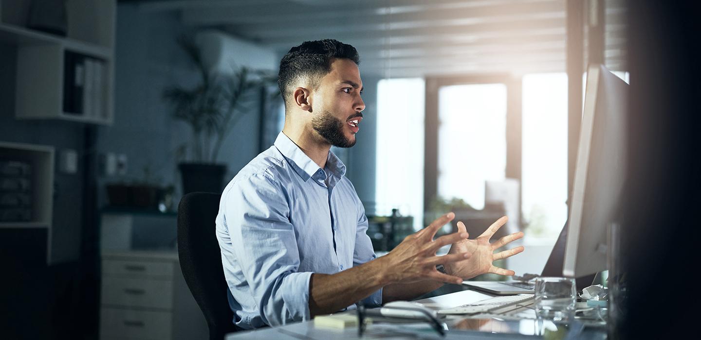 Frustrated man with blue shirt reacting to computer on his desk