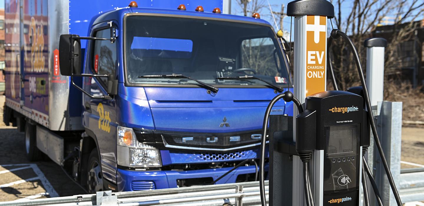 Blue Pitt box truck parked next to EV charging station.