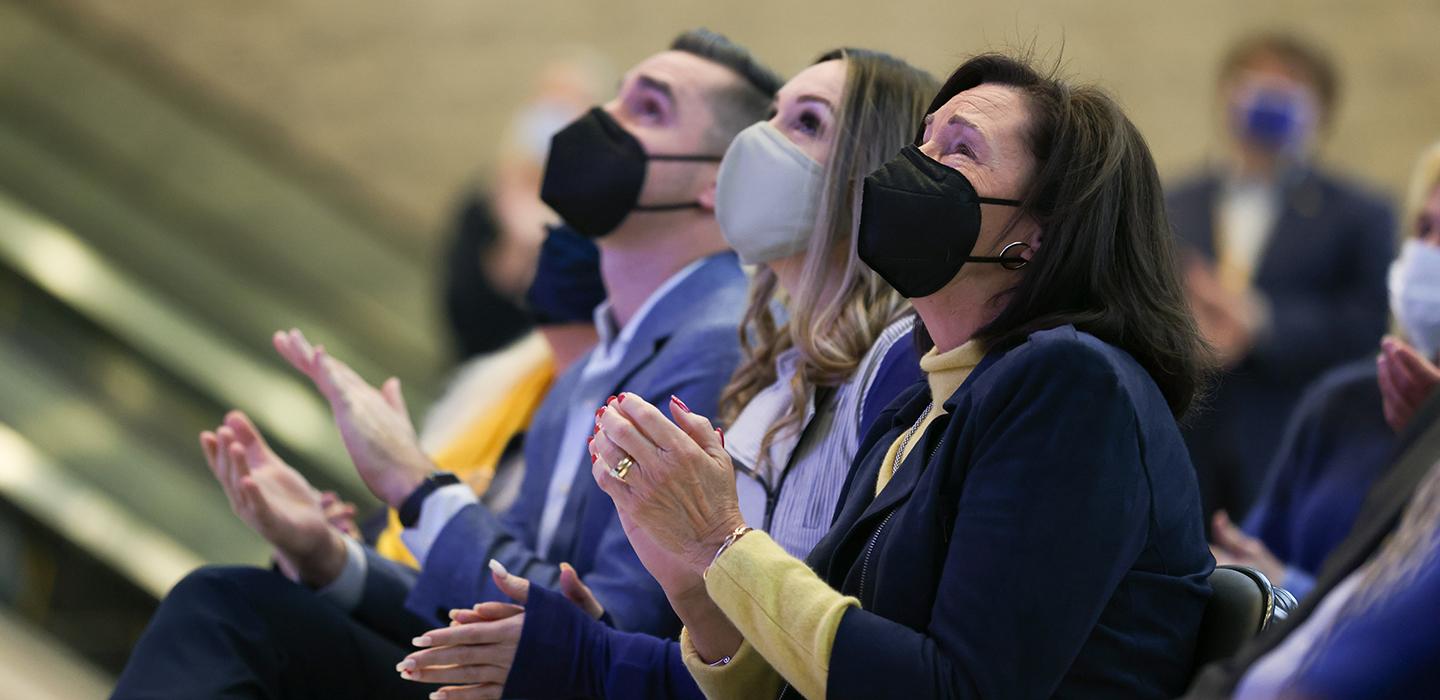 People wearing face masks indoors and clapping their hands