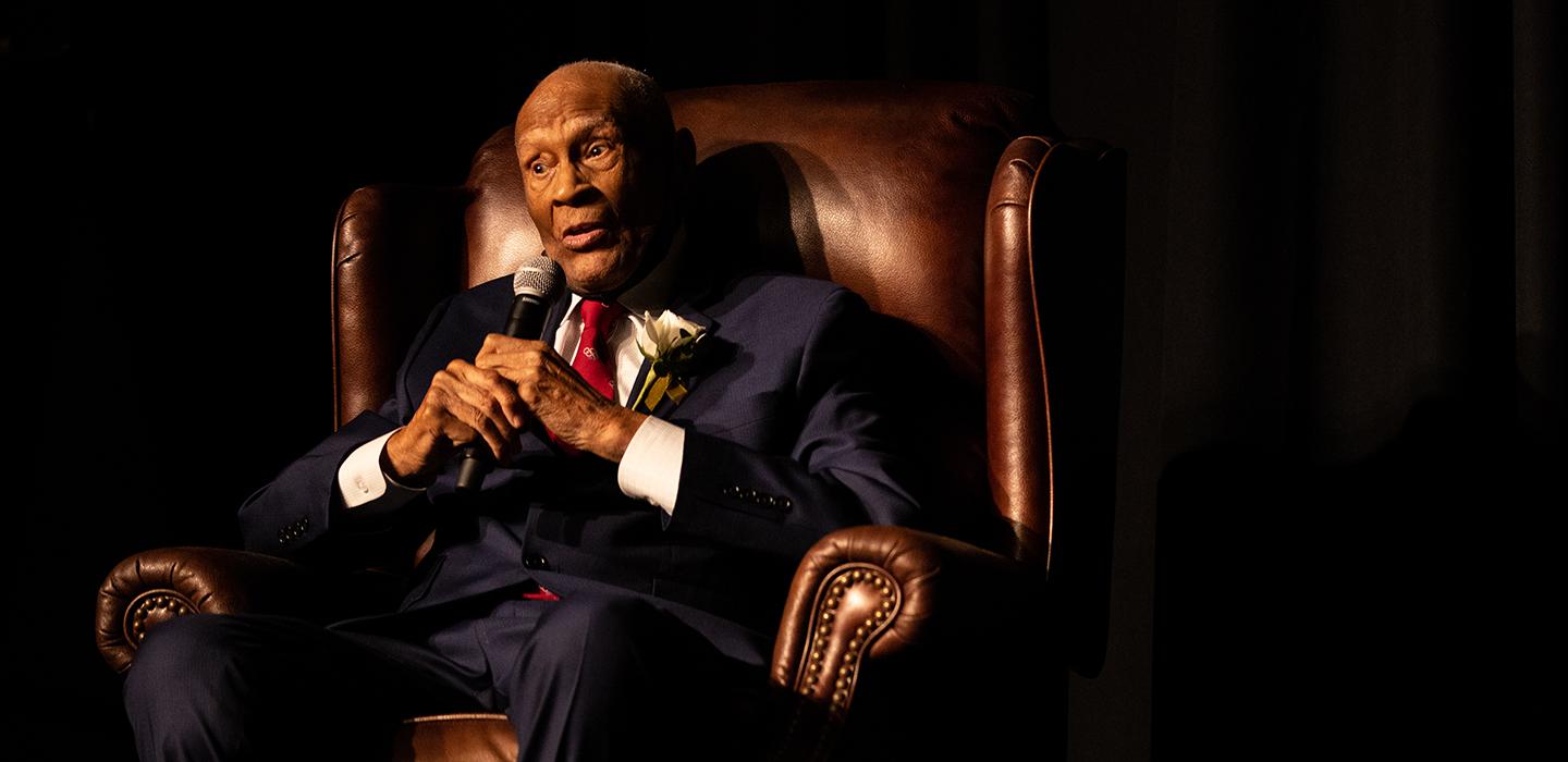 Herb Douglas sitting in a chair and speaking into microphone