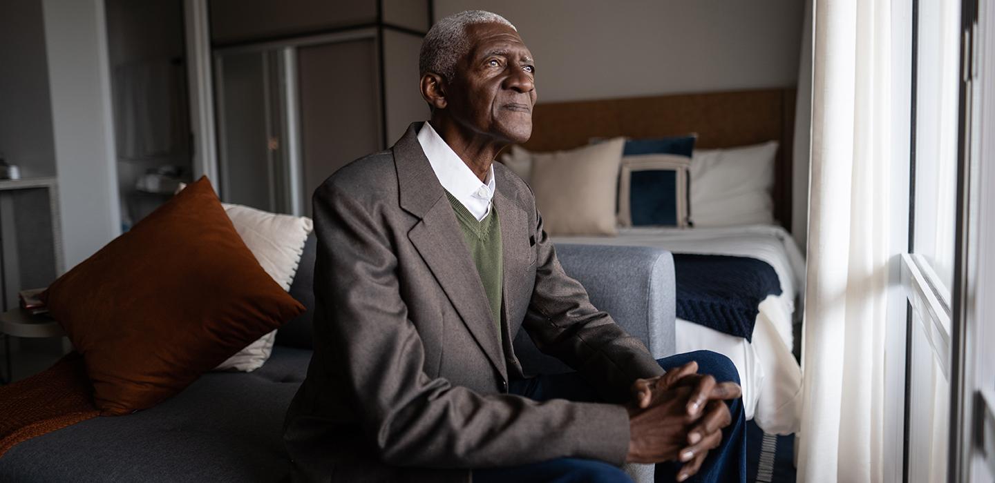 Elderly man in suit sitting on bed looking out of window