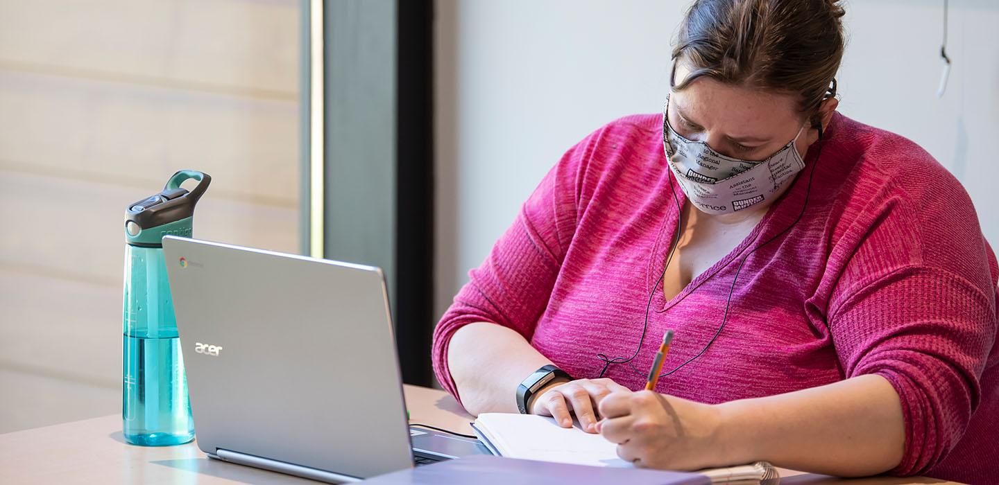 a person in a pink blouse studying at a laptop