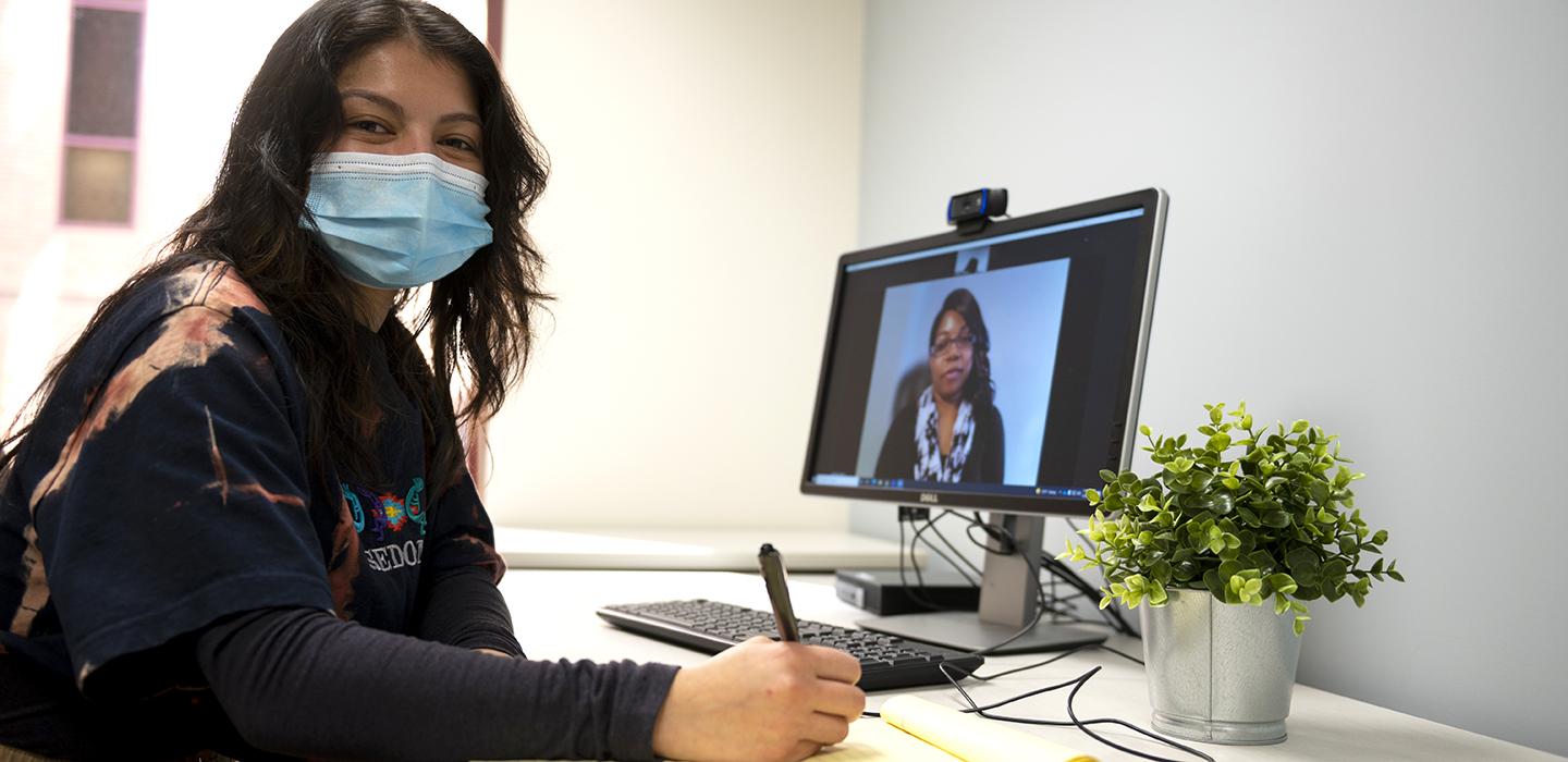 Woman sitting at desk and writing notes during video call 