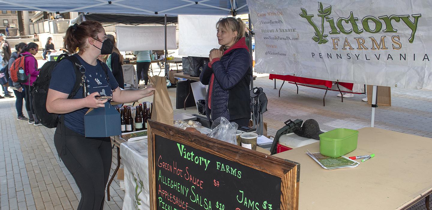 Student purchasing from Victory Farms stand at farmers market