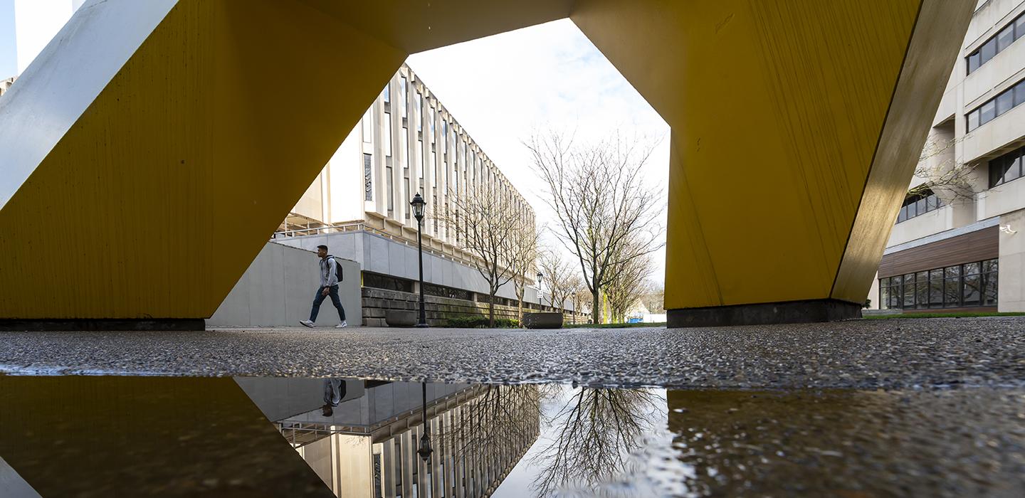 Student walking near large yellow sculpture on campus