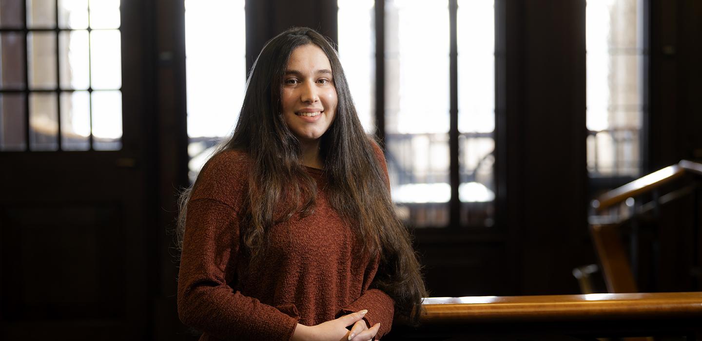 Katie Oppenheimer in brown sweater smiling in front of windows