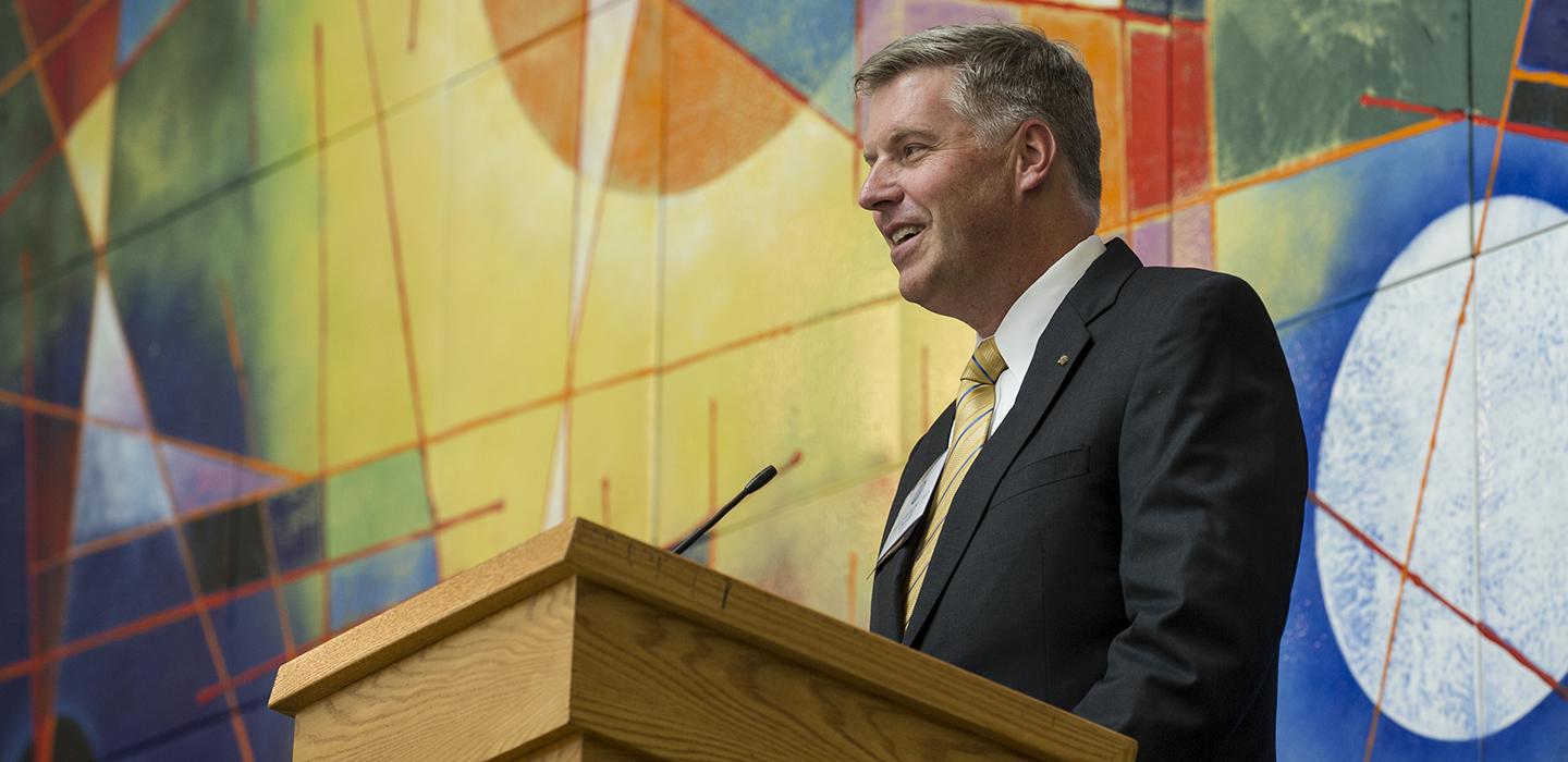 Chancellor Patrick Gallagher speaking at podium in front of colorful wall