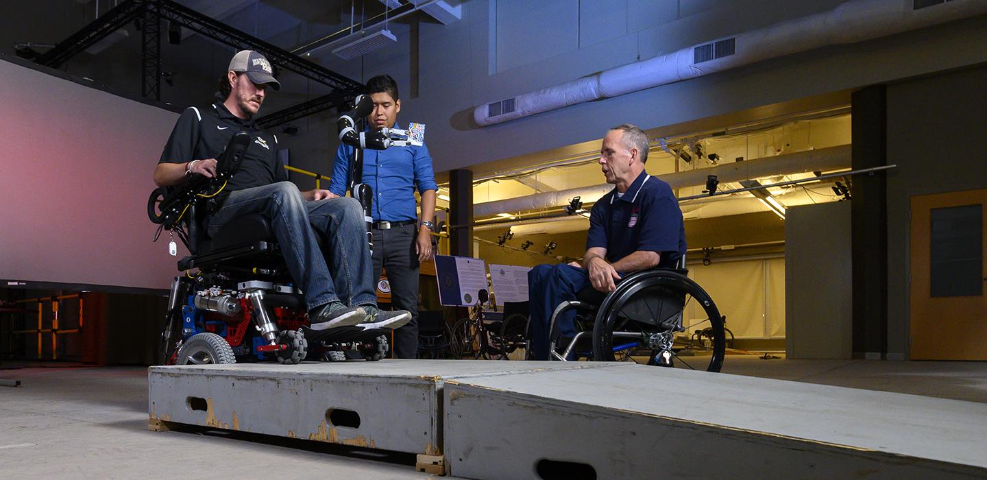 Man standing with two other men in wheelchairs 