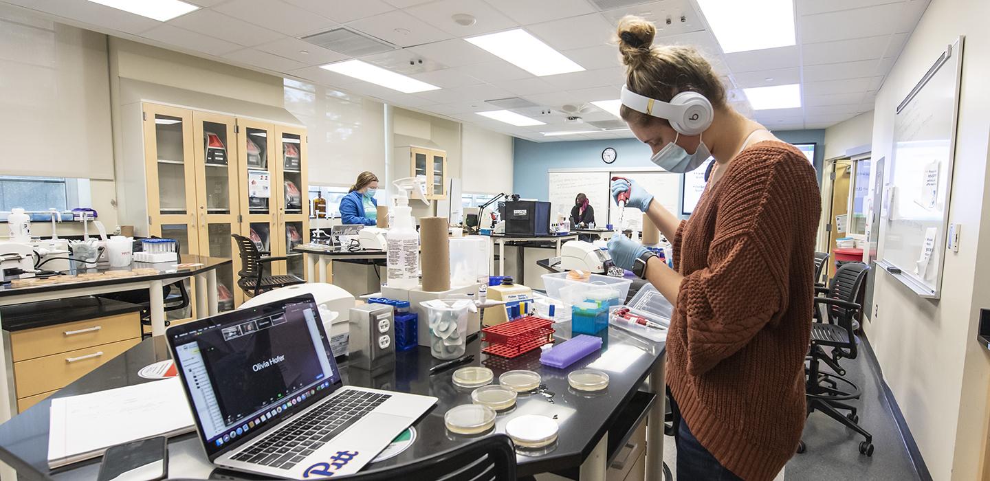 A person wearing headphones and a face mask in a brown sweater performs tests at a desk