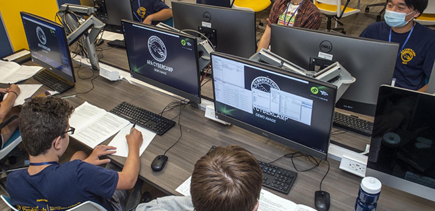 several kids at large computers with books in front of them