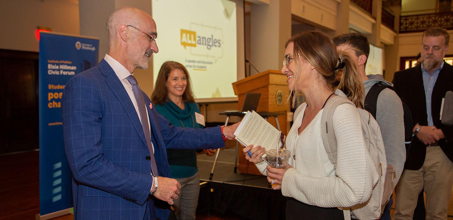 a man in a suit speaking to a student holding a book