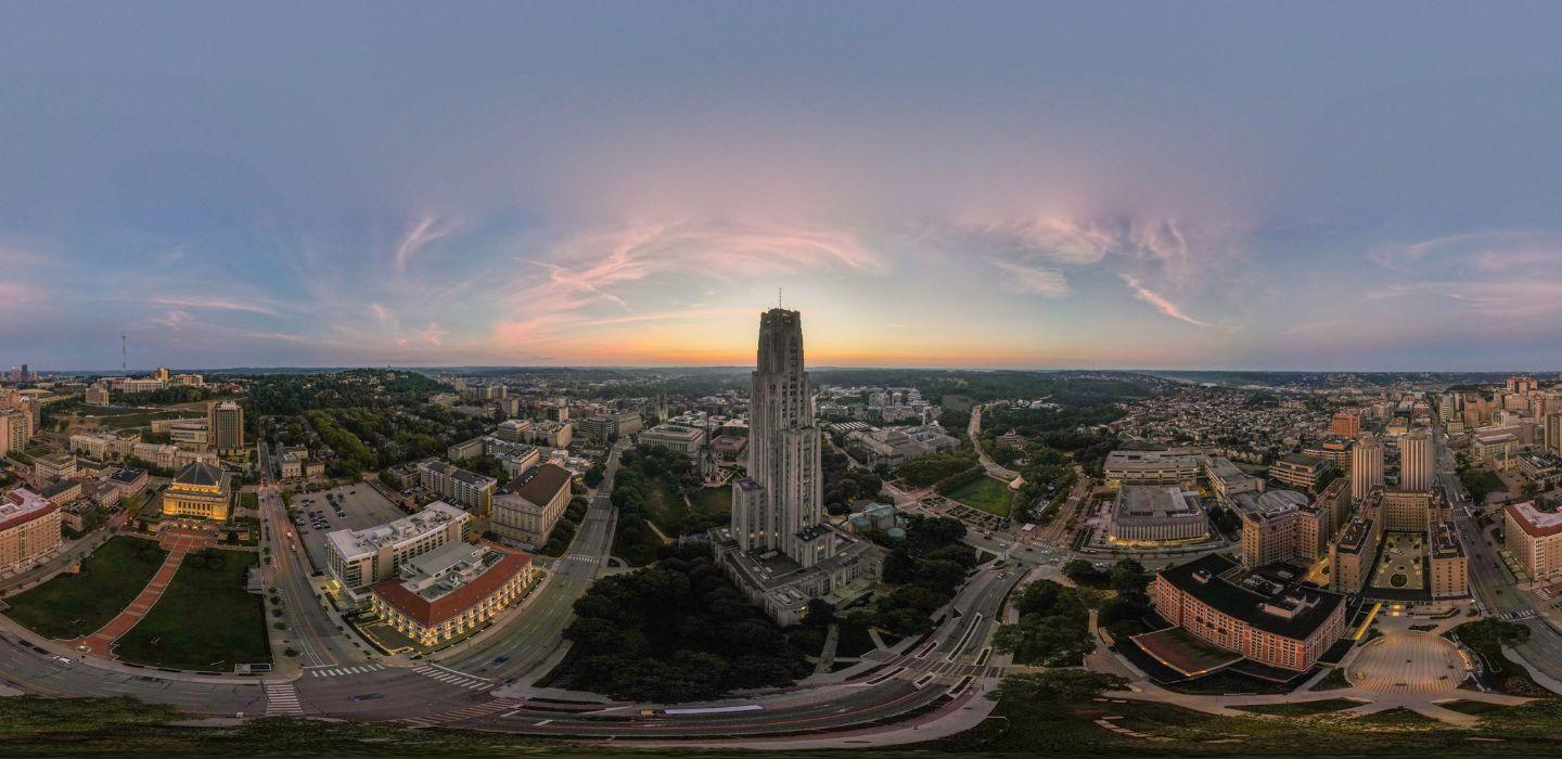 A drone shot shows the sun rising over the Oakland neighborhood and University of Pittsburgh campus, with the Cathedral of Learning in the center.