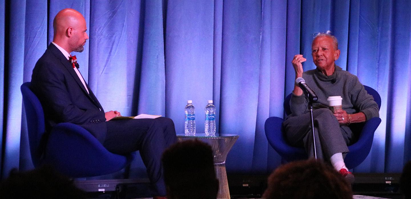 Pickett and Giovanni sit in blue chairs on a stage