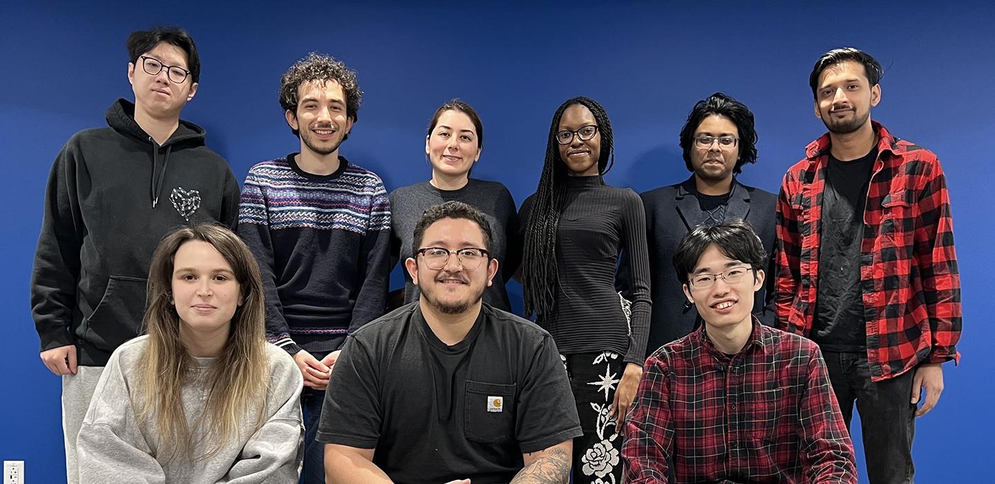 9 people pose against a blue wall