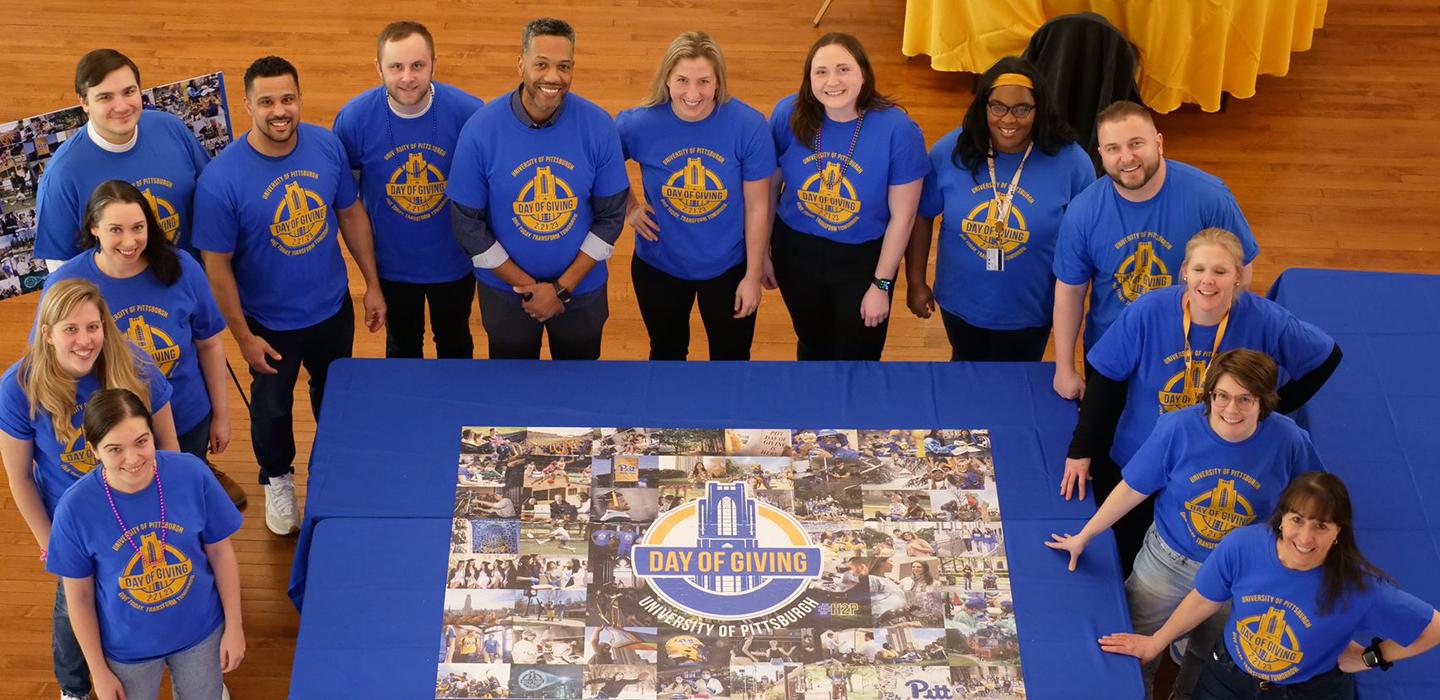 People in blue shirts gather around a Pitt Day of Giving puzzle